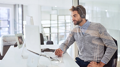 Person with headset at a computer represents online software demos, product presentations and expert support