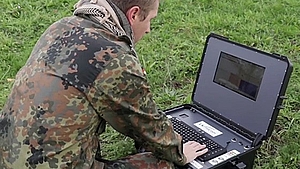 Soldier using a portable spectrum monitoring device in a field environment.