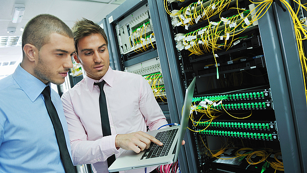 Two IT professionals analyzing a laptop screen in front of a server rack, representing LS telcom’s support services for network operations, troubleshooting, and training.